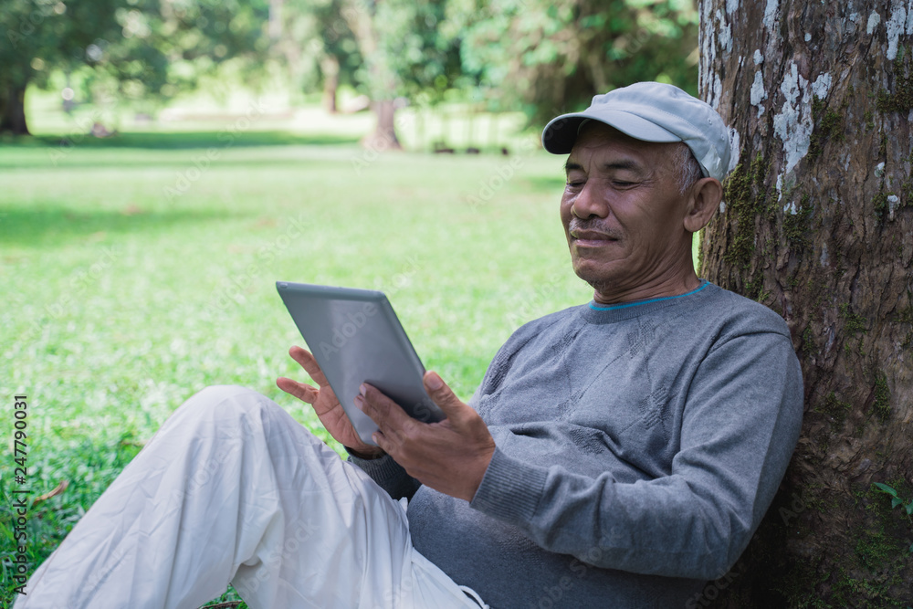 senior old man using tablet pc while relaxing in the park senior old man using tablet pc while relaxing in the park
