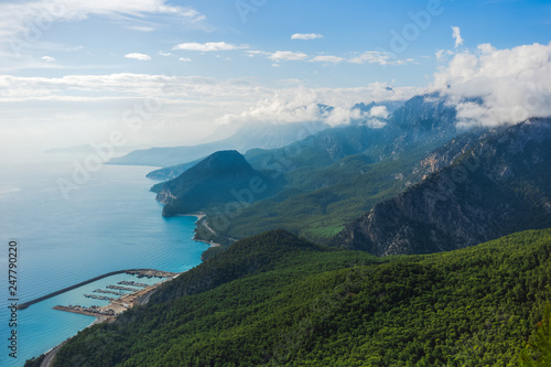 Beautiful sunny aerial view of Turkish marine landscape. Picturesque green mountains and fluffy white clouds over peaks. Charming nature background. Antalya city. Horizontal color photography.