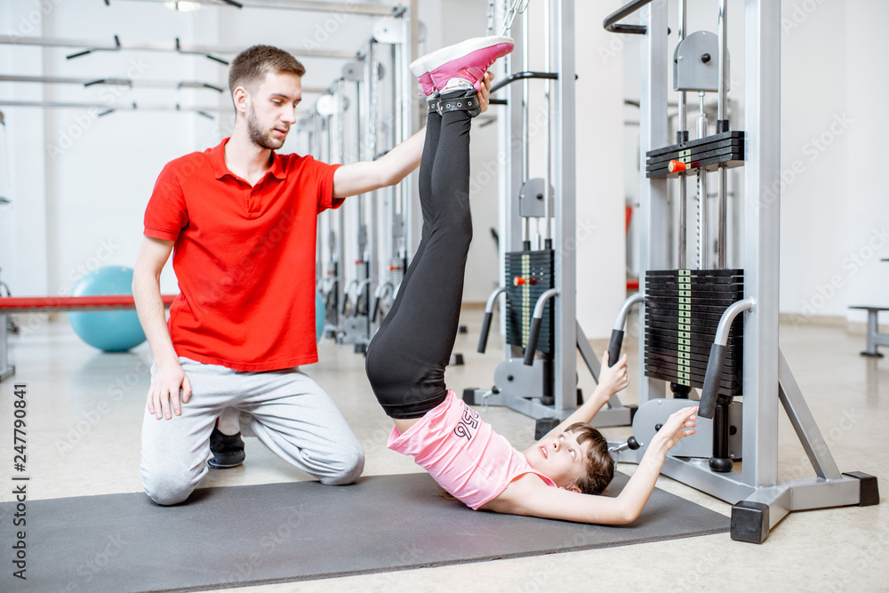 Fototapeta premium Young girl exercising on the decompression simulators with trainer during the spine treatment at the rehabilitation gym