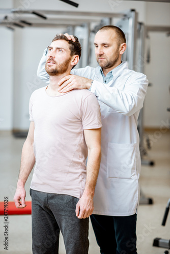 Professional senior physiotherapist doing manual treatment to a man standing in the rehabilitation gym