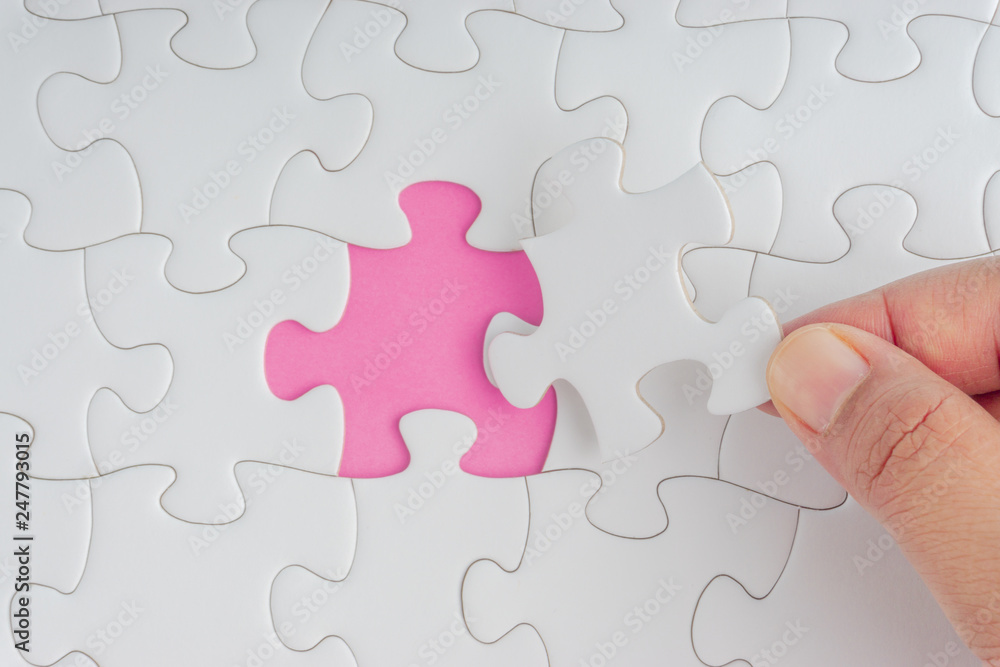 Hand put the last piece of jigsaw puzzle closeup to complete the mission. Selective focus and crop fragment