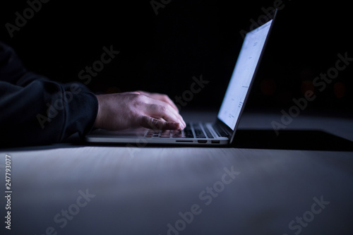 hacker using laptop computer while working in dark office