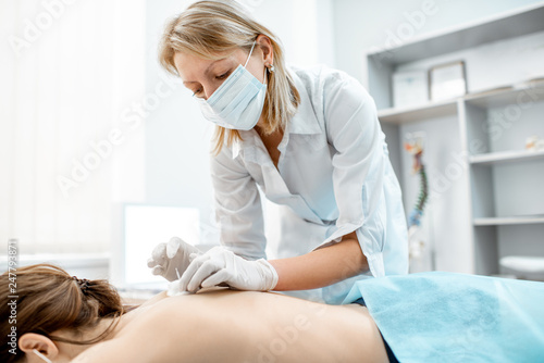 Neuropathologist puts needles into the woman's back removing inflammation of the muscles during the acupuncture treatment in the office