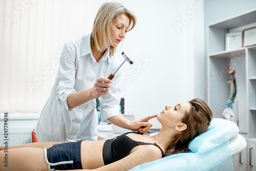 Young woman during the medical examination with neurologist testing reflexes with hammer in the office photo