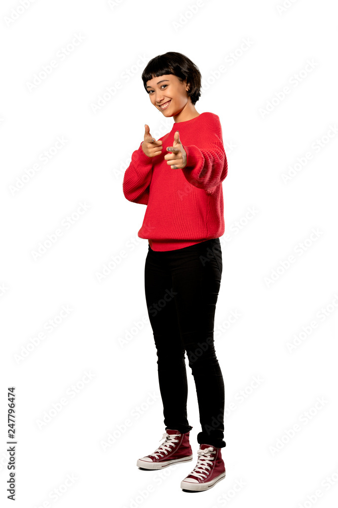 A full-length shot of a Short hair girl with red sweater pointing to the front and smiling over isolated white background A full-length shot of a Short hair girl with red sweater pointing to the front and smiling over isolated white background