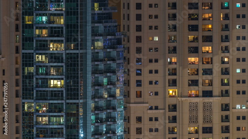 Glowing windows in multistory modern glass residential building light up at night timelapse.