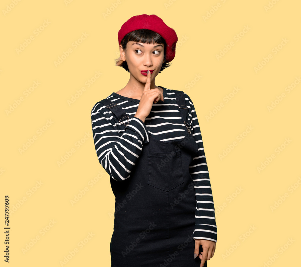 Young woman with beret showing a sign of silence gesture over yellow background Young woman with beret showing a sign of silence gesture over yellow background