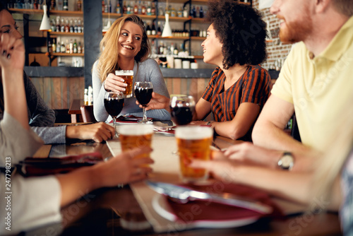Multicultural friends sitting in restaurant and drinking wine and beer.