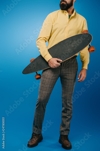 cropped view of man holding skateboard isolated on blue photo