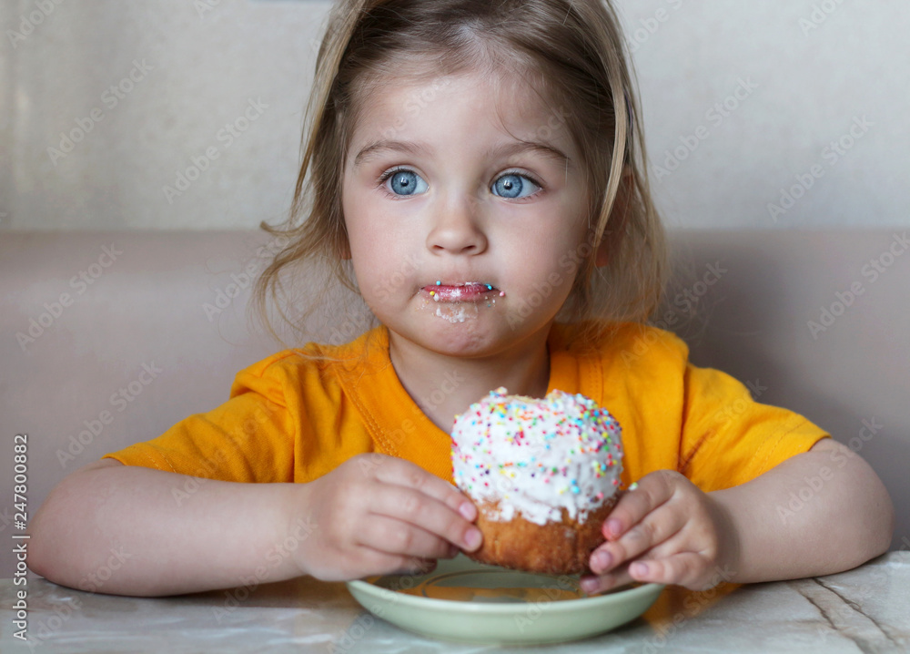 A cute little baby is sitting at a table eating a bun. Child with blue eyes A cute little baby is sitting at a table eating a bun. Child with blue eyes