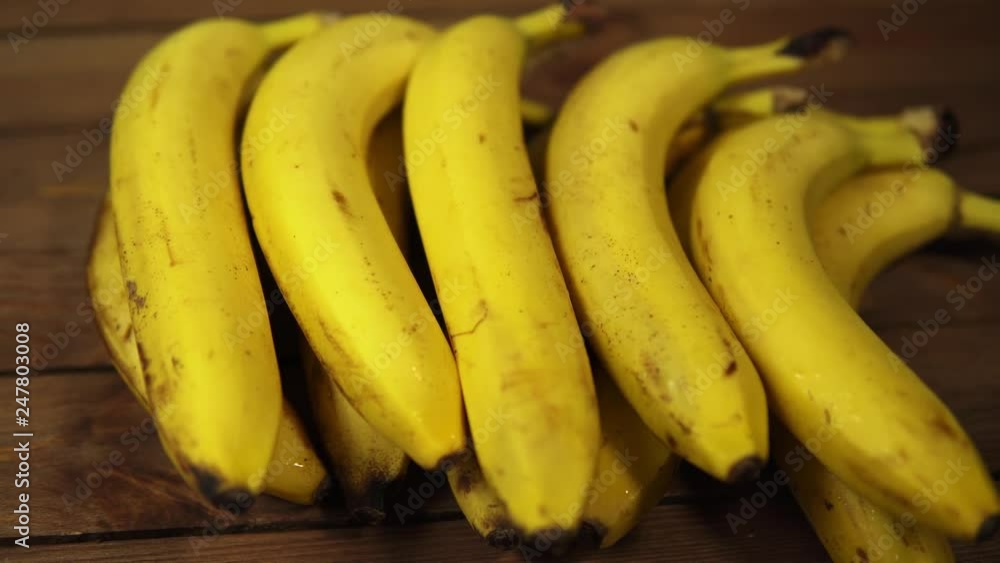 A bunch of yellow ripe mouth-watering bananas lie on a wooden table, the fruits are covered with water drops, dolly shot. A bunch of yellow ripe mouth-watering bananas lie on a wooden table, the fruits are covered with water drops, dolly shot.