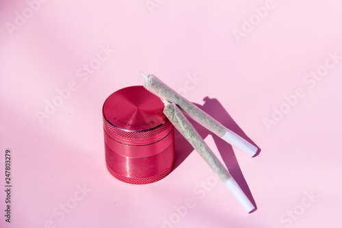 Pink cannabis grinder with two cannabis joints pink background photo