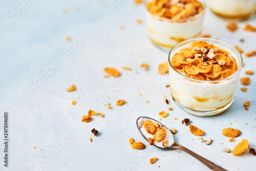 Healthy breakfast or dessert. Tasty corn flakes with yogurt, almond and honey in a small glass on light blue background. Copy space for text.