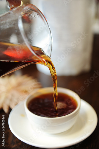 Pour freshly brewed black tea from a glass jug into a ceramic tea bowl