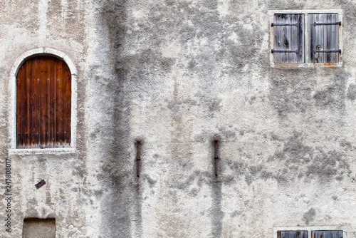 A fragment of a very old abandoned house with a closed door and a shuttered blind window.