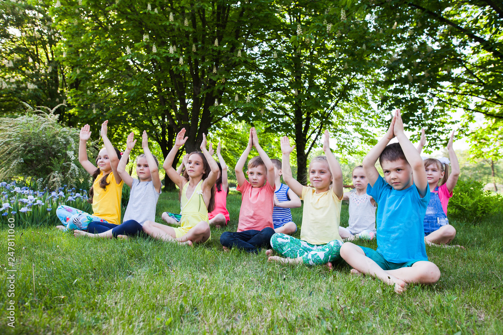 A large group of children engaged in yoga in the Park sitting on the grass. A large group of children engaged in yoga in the Park sitting on the grass.