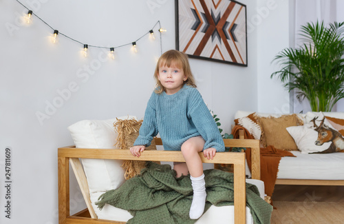 Portrait of little girl in blue sweater, sitting at armchair, looking at camera, smiling.