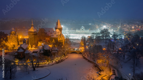 Budapest, Hungary - Aerial view of the beautiful snowy Vajdahunyad Castle at blue hour with Christmas market, ice rink and Heroes' Square at background