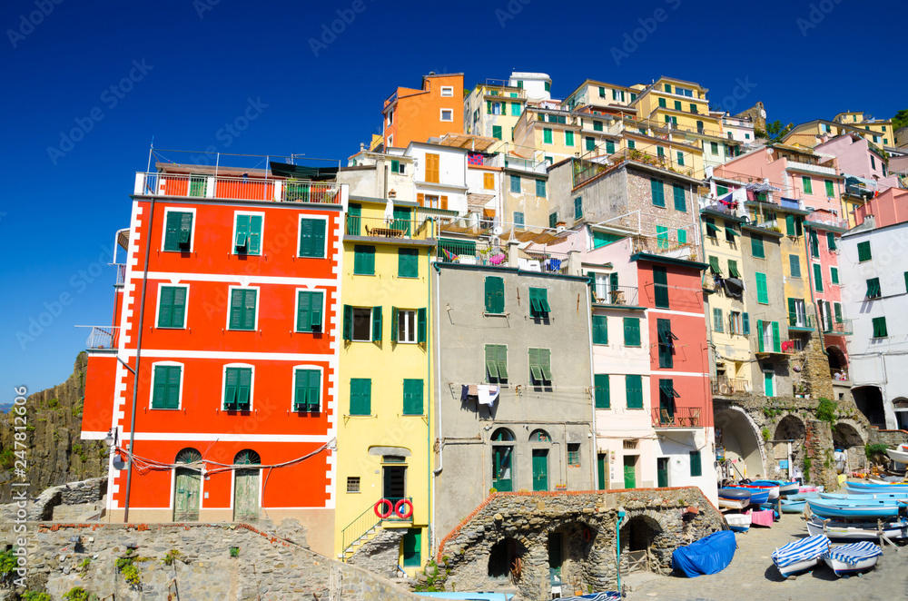 Riomaggiore traditional typical Italian fishing village in National park Cinque Terre with colorful multicolored buildings houses close-up on hill and boats, clear blue sky background, Liguria, Italy