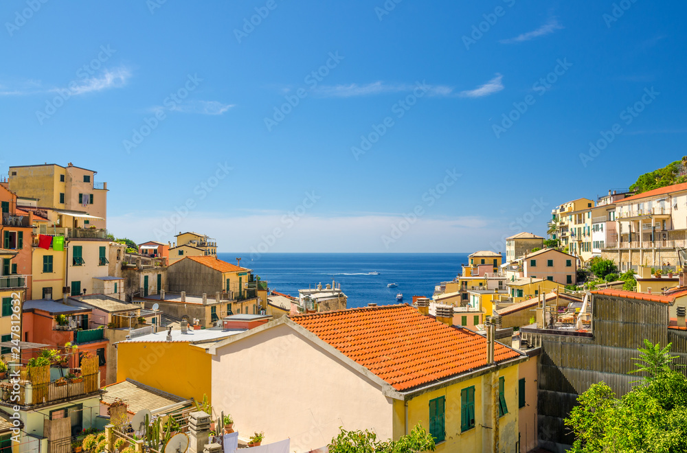 Top view of orange tiled roofs of multicolored houses with balconies and shutter windows of Riomaggiore typical fishing village National park Cinque Terre, horizon Ligurian Sea, Liguria, Italy