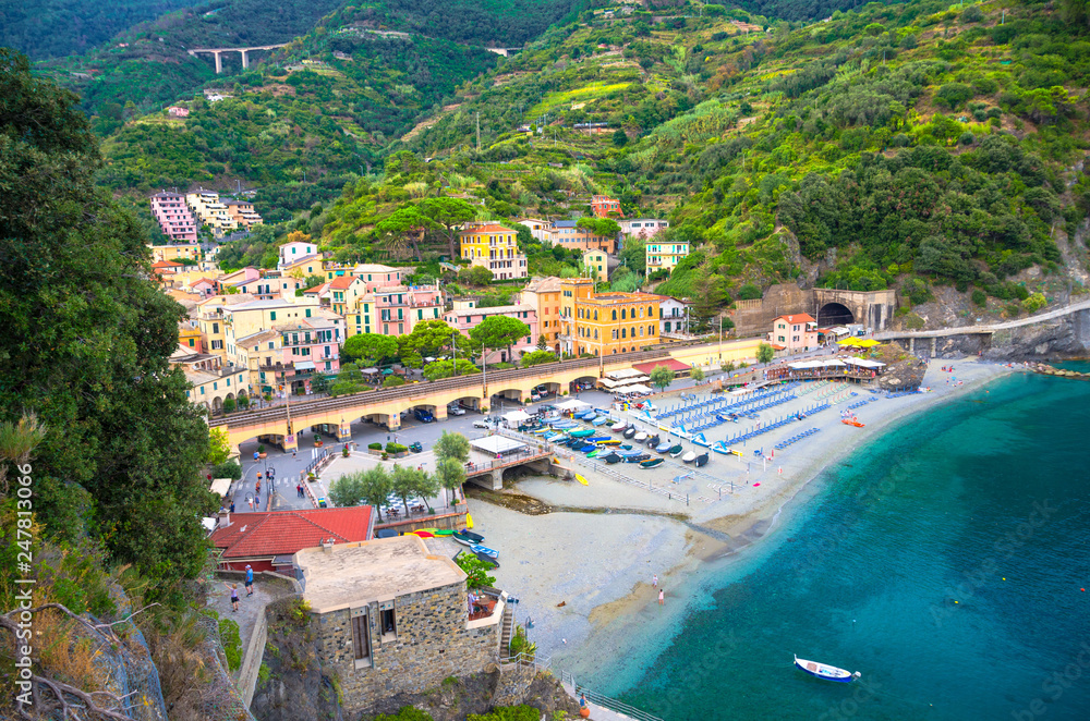 Top aerial view of green hill, railway, beach and harbor of Monterosso town village at sunset dusk, Genoa Gulf, Ligurian Sea, National park Cinque Terre, La Spezia, Liguria, Italy