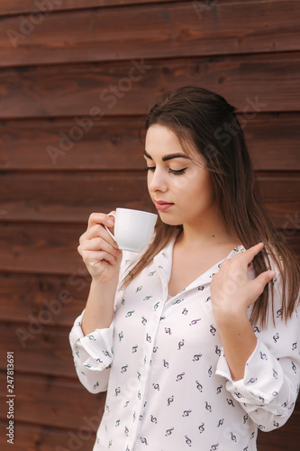 Beautiful girl hold a cup of coffee. White shirt. Wooden background