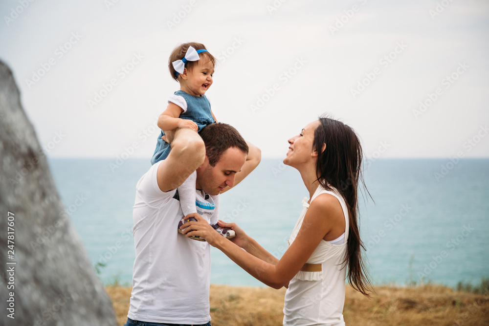 Happy young family in white t-shirts and blue jeans with a small daughter in dress near to the lighthouse, playing together Happy young family in white t-shirts and blue jeans with a small daughter in dress near to the lighthouse, playing together