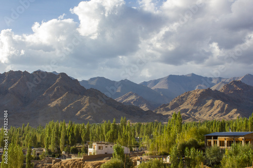 village houses in a green forest against the backdrop of desert mountains under heavy clouds