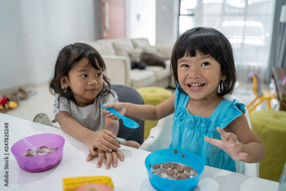 happy two little asian girls having breakfast together in the kitchen at home