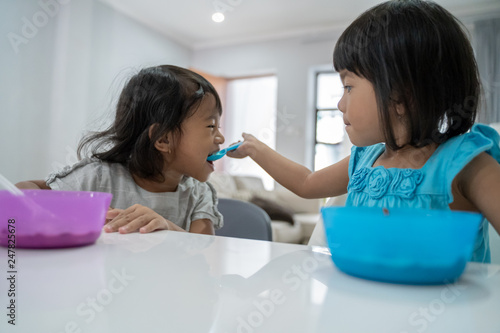 cute little girl sister feeding each other while having breakfast at home in the morning