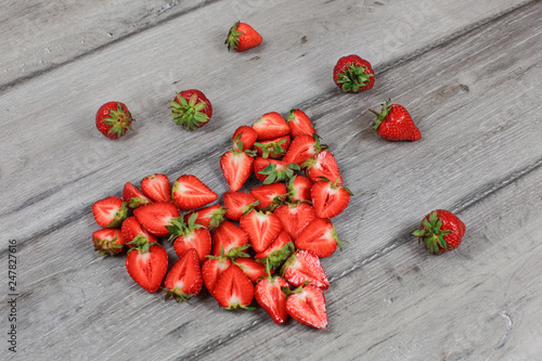 Strawberries cut to pieces arranged in shape of hear on gray wood desk.