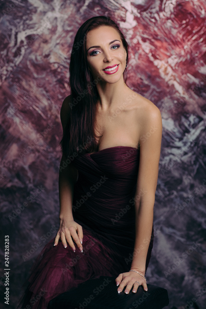 Portrait of magnificent sexy woman in evening dress posing over dark red background Portrait of magnificent sexy woman in evening dress posing over dark red background