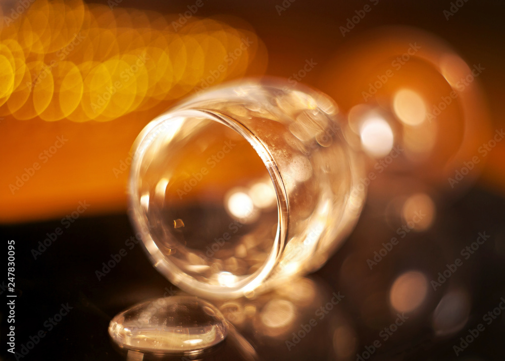 The glass lying on the table with spilled liquid with a reflection on the blurred  background of the New Year's garland with bokeh