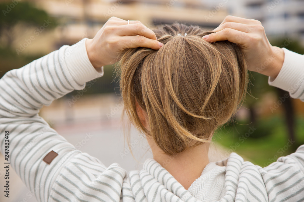 Naklejka premium Back view of woman tying hair in ponytail and wearing sportswear