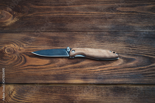 hunting bowie knife with a wooden handle on dark wooden background. Steel arms weapon. top view