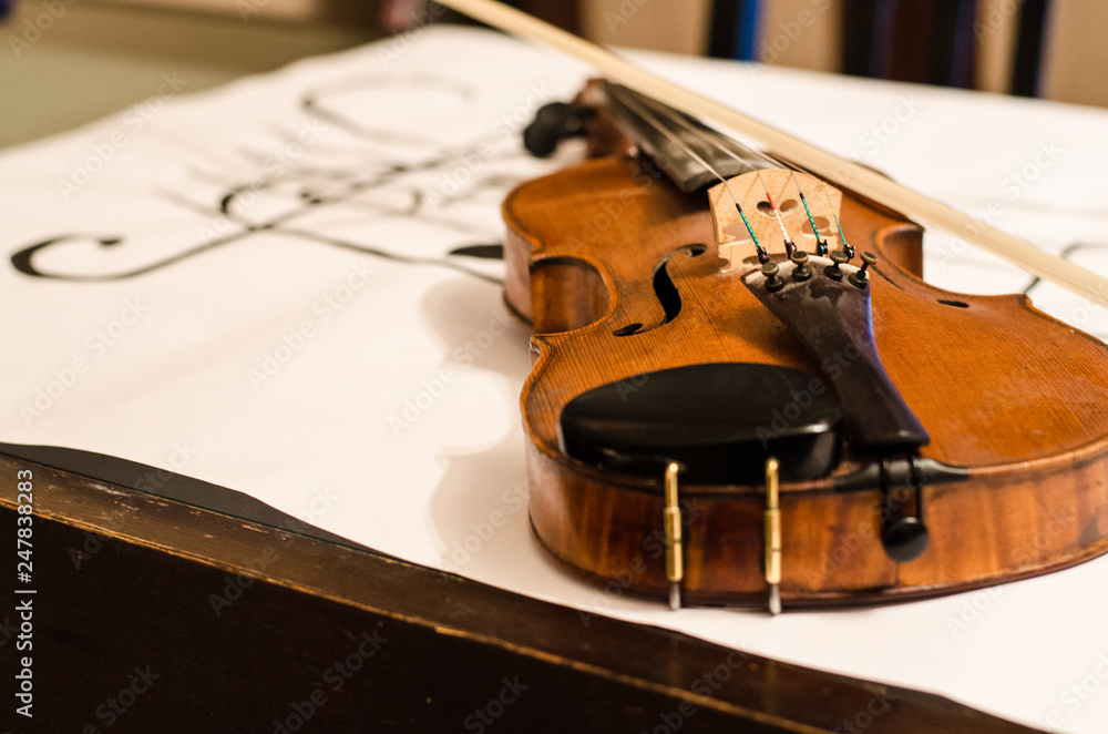 Fototapeta premium Close up of Violin body with bow positioned in a diagonal over a musical stave drawing with a G-clef with musical notes on a white background