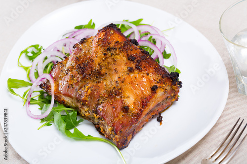 Baked under sauce tasty pork ribs at plate with arugula and onion