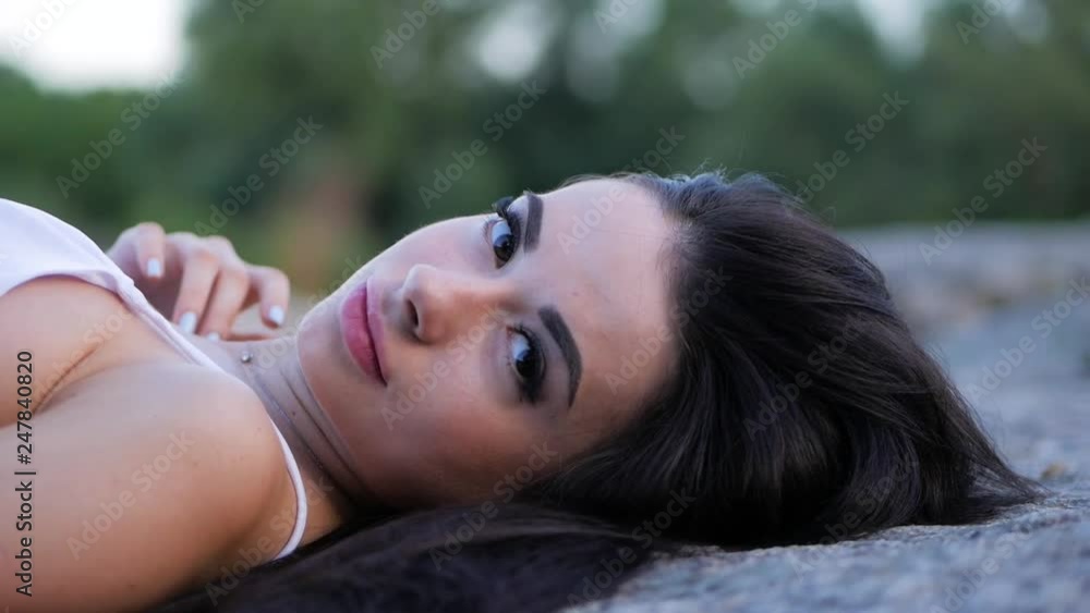 Pretty brunette girl with long hair posing for the camera lying on a rock Pretty brunette girl with long hair posing for the camera lying on a rock
