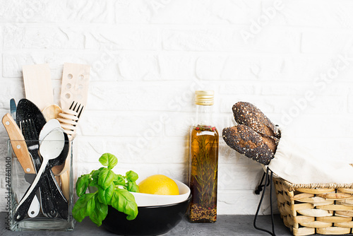 Kitchen tools, olive cutting boan a kitchen shelf against a white brick wall. Fresh basil and lemon. White and black modern cutlery. No plastic house photo