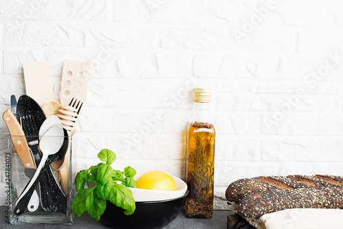 Kitchen tools, olive cutting boan a kitchen shelf against a white brick wall. Fresh basil and lemon. White and black modern cutlery. No plastic house photo