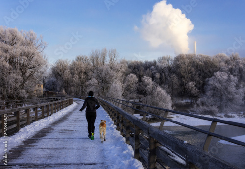 Joggerin mit Hund im Winter auf einer verschneiten Brücke