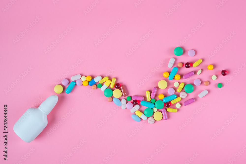 White, yellow, red, blue pills, tablets and white bottle on pink background White, yellow, red, blue pills, tablets and white bottle on pink background