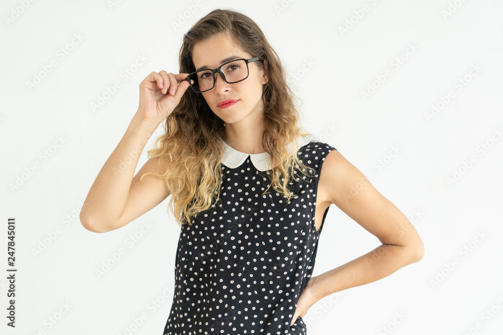 Serious woman adjusting glasses and keeping hand on hip Serious woman adjusting glasses and keeping hand on hip
