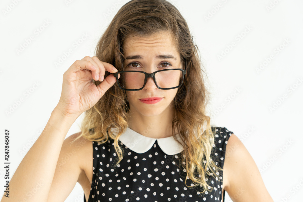 Skeptical pretty young woman looking at camera over glasses