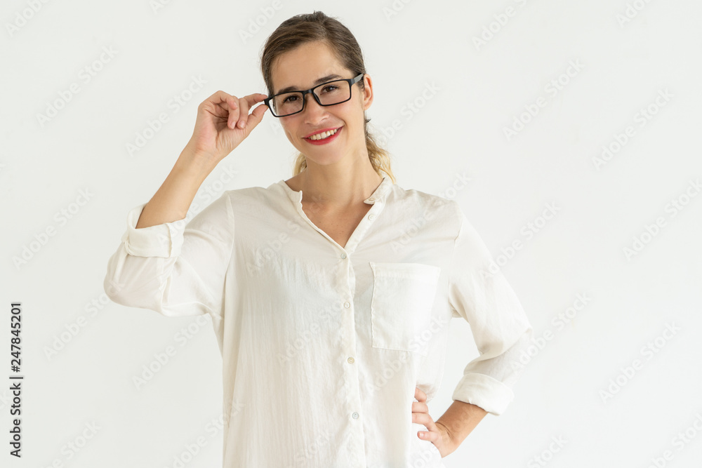 Smiling woman adjusting glasses and keeping hand on hip Smiling woman adjusting glasses and keeping hand on hip