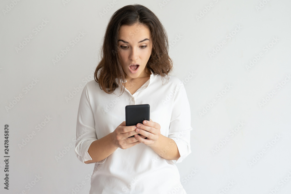 Shocked woman holding smartphone and looking at its screen Shocked woman holding smartphone and looking at its screen