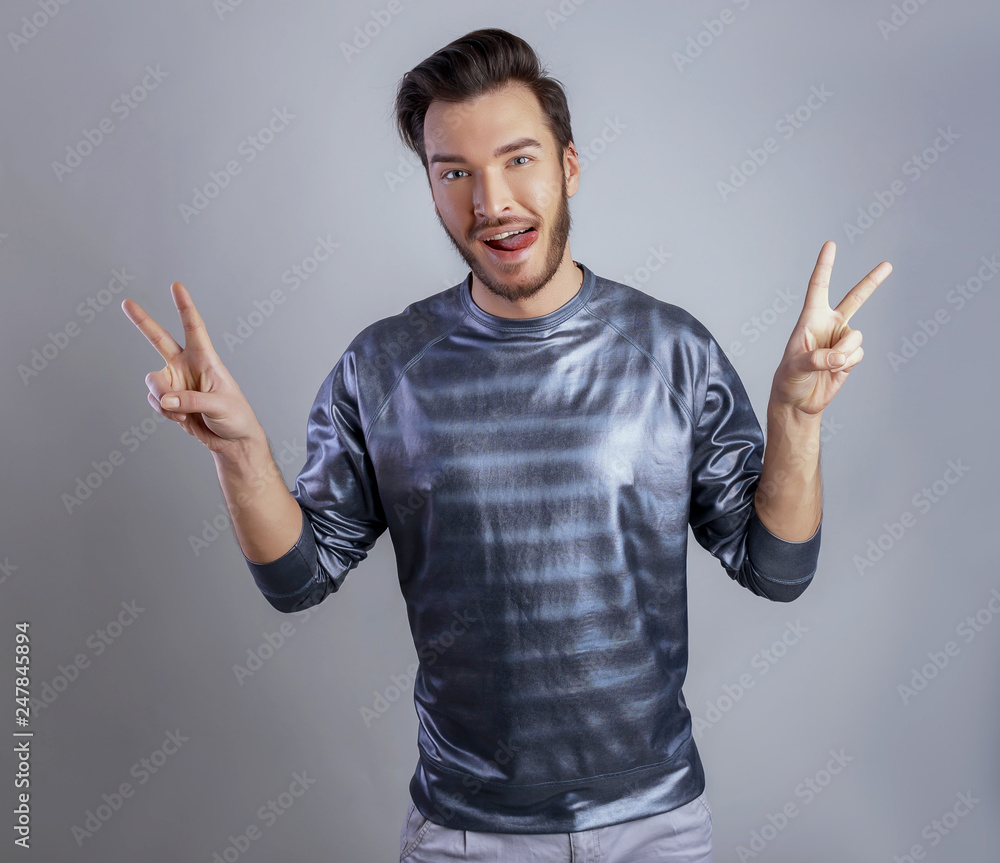 Happy and cheerful bearded hipster man in casual clothes showing peace or victory symbol gesture both hands. Man opened wide mouth showing tongue Happy and cheerful bearded hipster man in casual clothes showing peace or victory symbol gesture both hands. Man opened wide mouth showing tongue