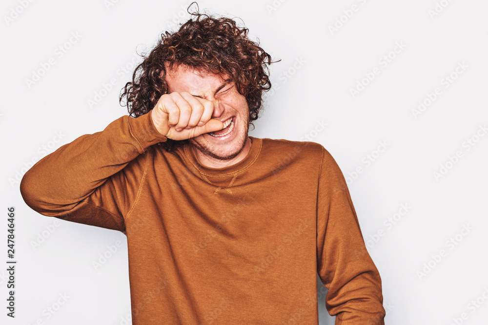 Studio shot of handsome freckled positive male is laughing wiping his eyes posing for social advertisement, isolated on white background with blank copy space for your promotional information. Studio shot of handsome freckled positive male is laughing wiping his eyes posing for social advertisement, isolated on white background with blank copy space for your promotional information.