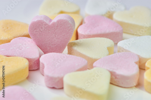 macro color photo of candy hearts lying on white background, one pink heart is standing, copy space