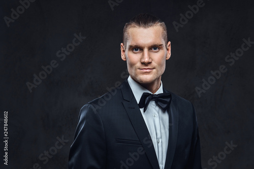 Portrait of a handsome stylish wearing elegant classical suit with a bow tie. Studio shot on a dark textured wall © Fxquadro